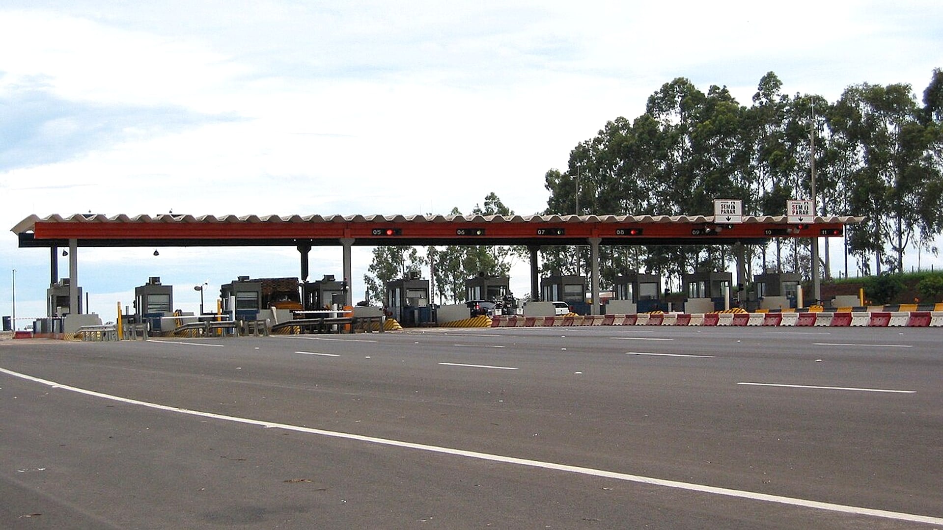 Praça de pedágio de uma rodovia brasileira vista de lado, com as cabines alinhadas sob o céu claro