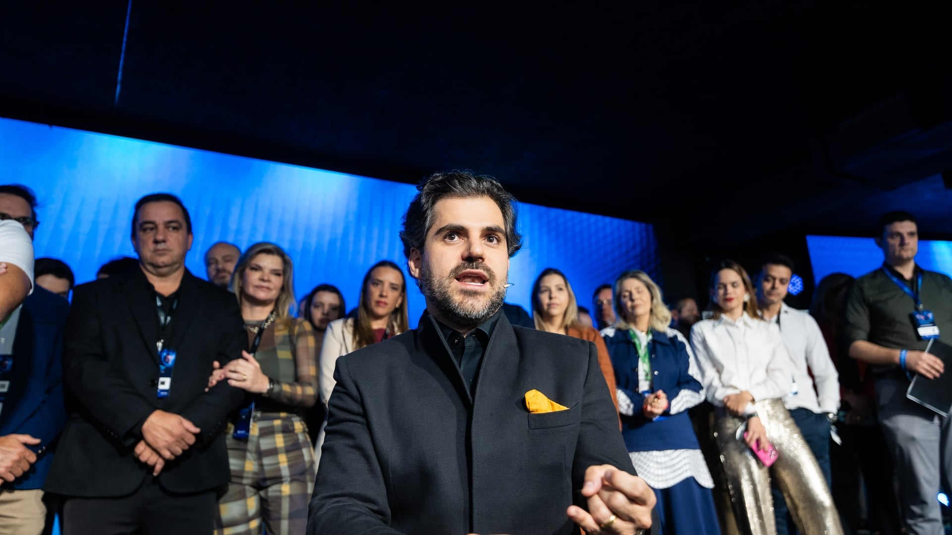Samuel Pereira falando no meio da plateia durante o Segredos da Odontologia, com participantes em pé atrás dele