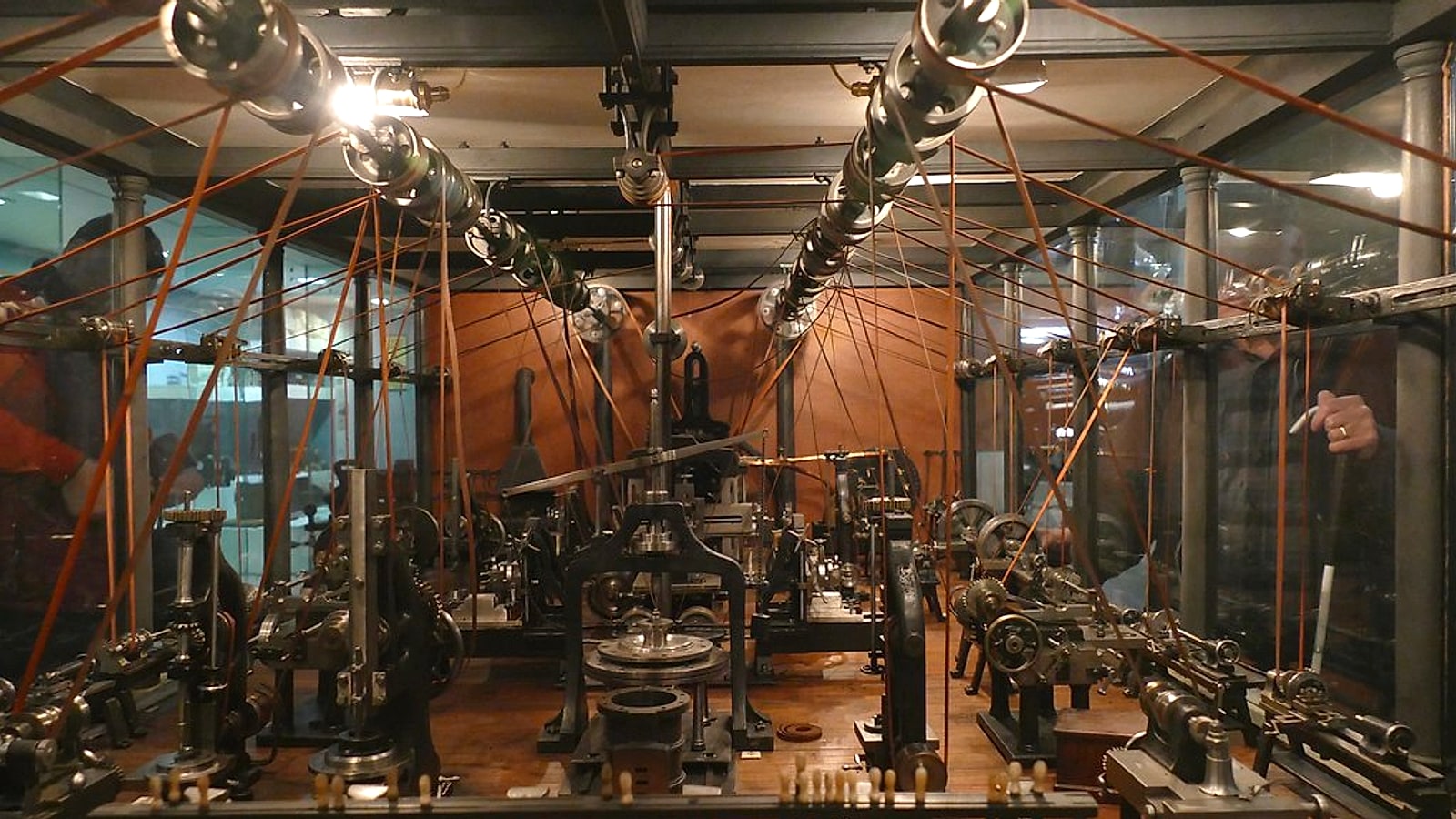 Maquete de uma oficina mecânica vitoriana no Science Museum de Londres, com eixos de transmissão no teto e dezenas de correias descendo até as máquinas