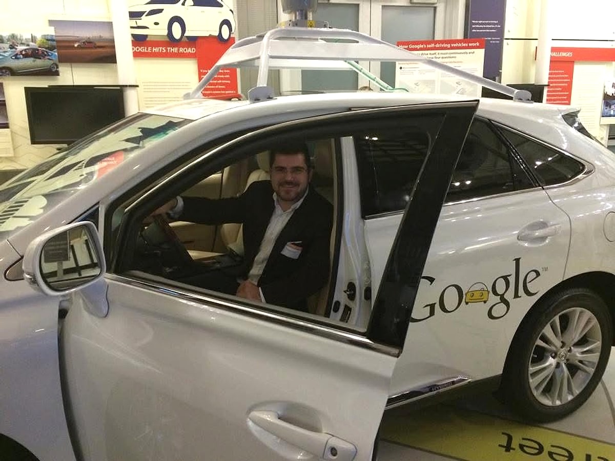 Samuel Pereira sentado dentro do carro autônomo do Google, um Lexus RX450h branco com sensor giratório no teto, durante visita ao Vale do Silício em 2014