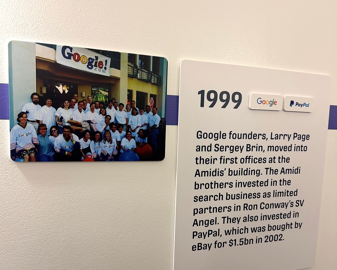 Placa na parede do Plug and Play contando que Larry Page e Sergey Brin montaram os primeiros escritórios do Google no prédio dos irmãos Amidi em 1999, ao lado da foto da equipe original do Google