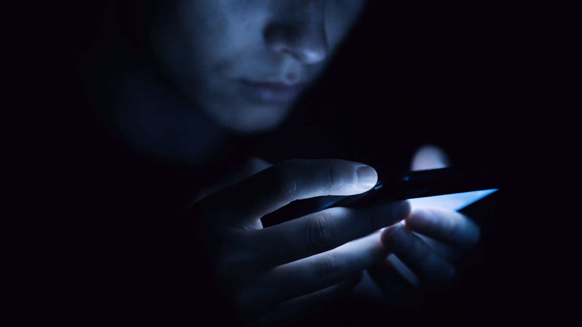 Pessoa no escuro com o rosto iluminado pela tela do celular, lendo a resposta de uma busca