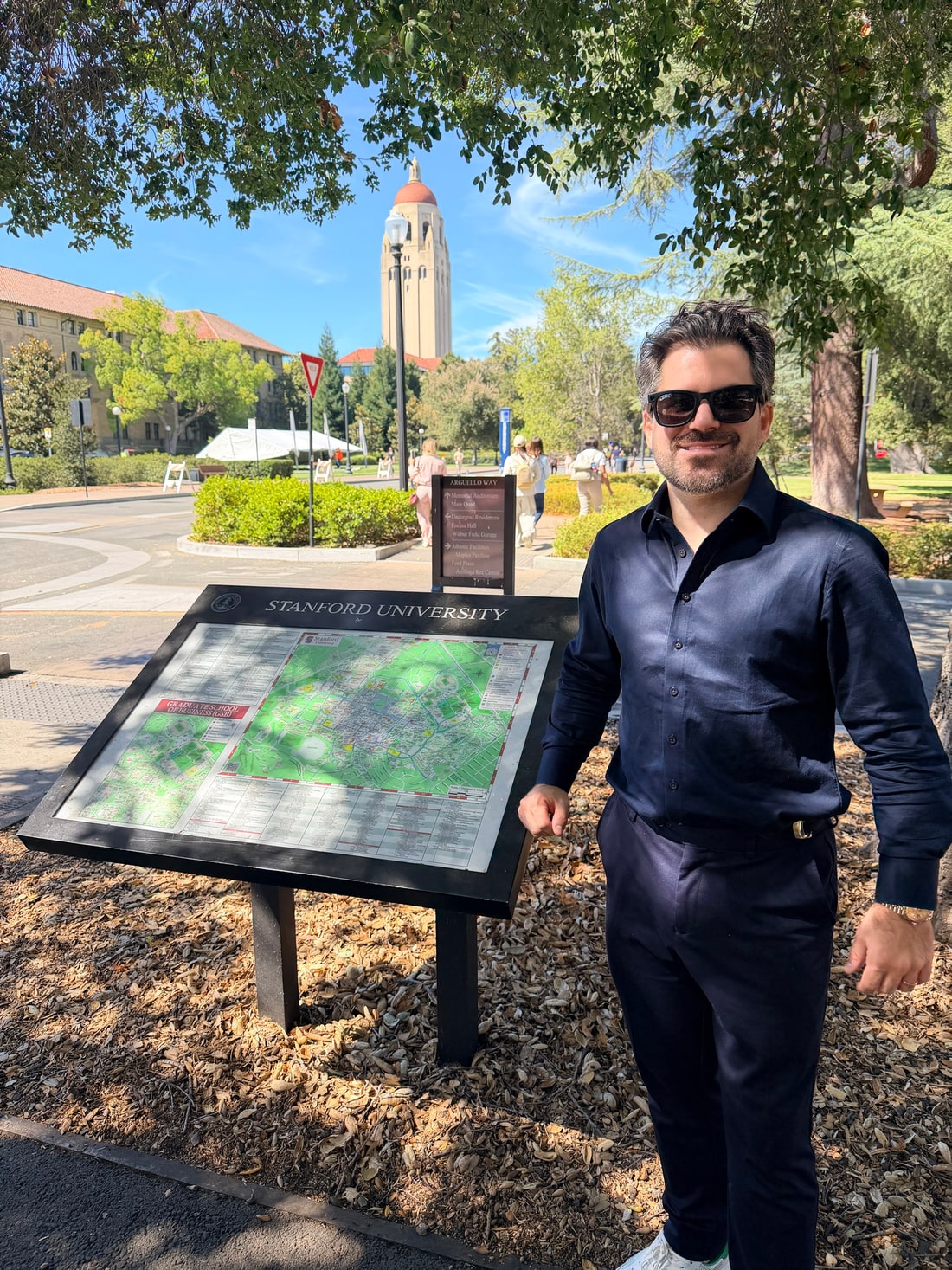 Samuel Pereira ao lado do mapa oficial do campus da Stanford University, com a Hoover Tower ao fundo, em Palo Alto, na Califórnia
