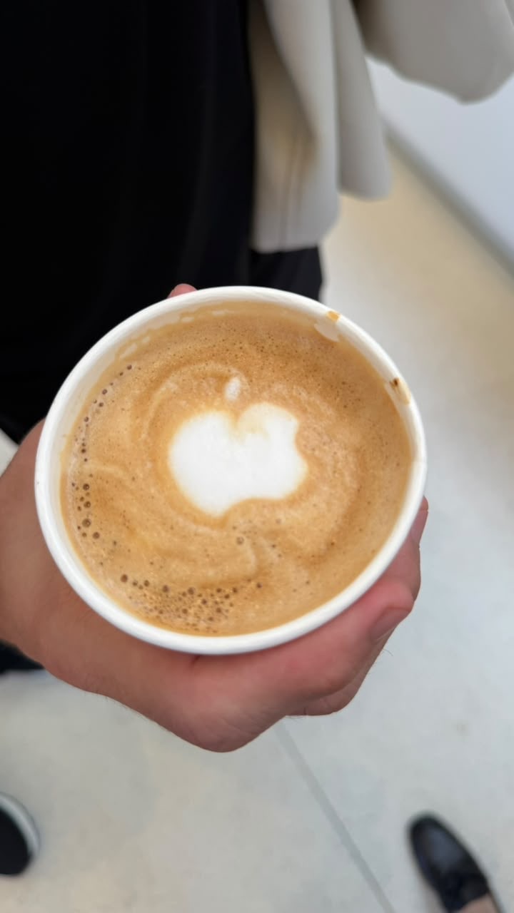 Copo de café com desenho da maçã da Apple feito na espuma, segurado por uma mão no Apple Park Visitor Center