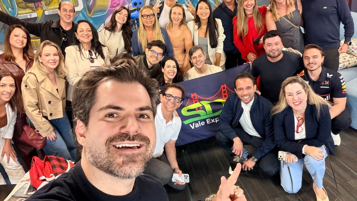 Selfie do grupo do SDA Vale Experience dentro do Circuit Launch, em Oakland, com a bandeira do grupo e um mural colorido ao fundo