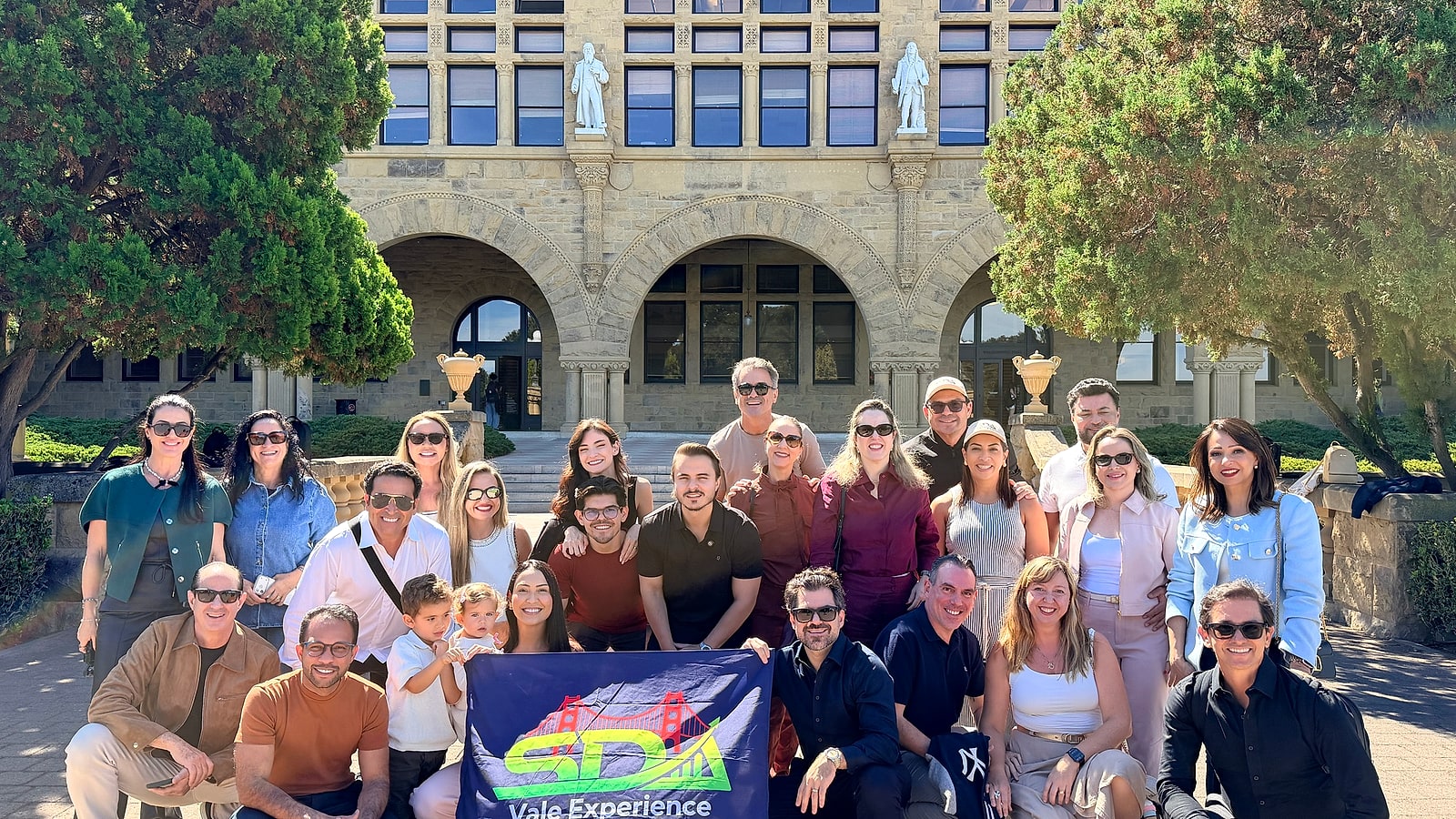 Grupo do SDA Vale Experience reunido diante de um dos prédios históricos do campus de Stanford, em Palo Alto, com a bandeira do grupo
