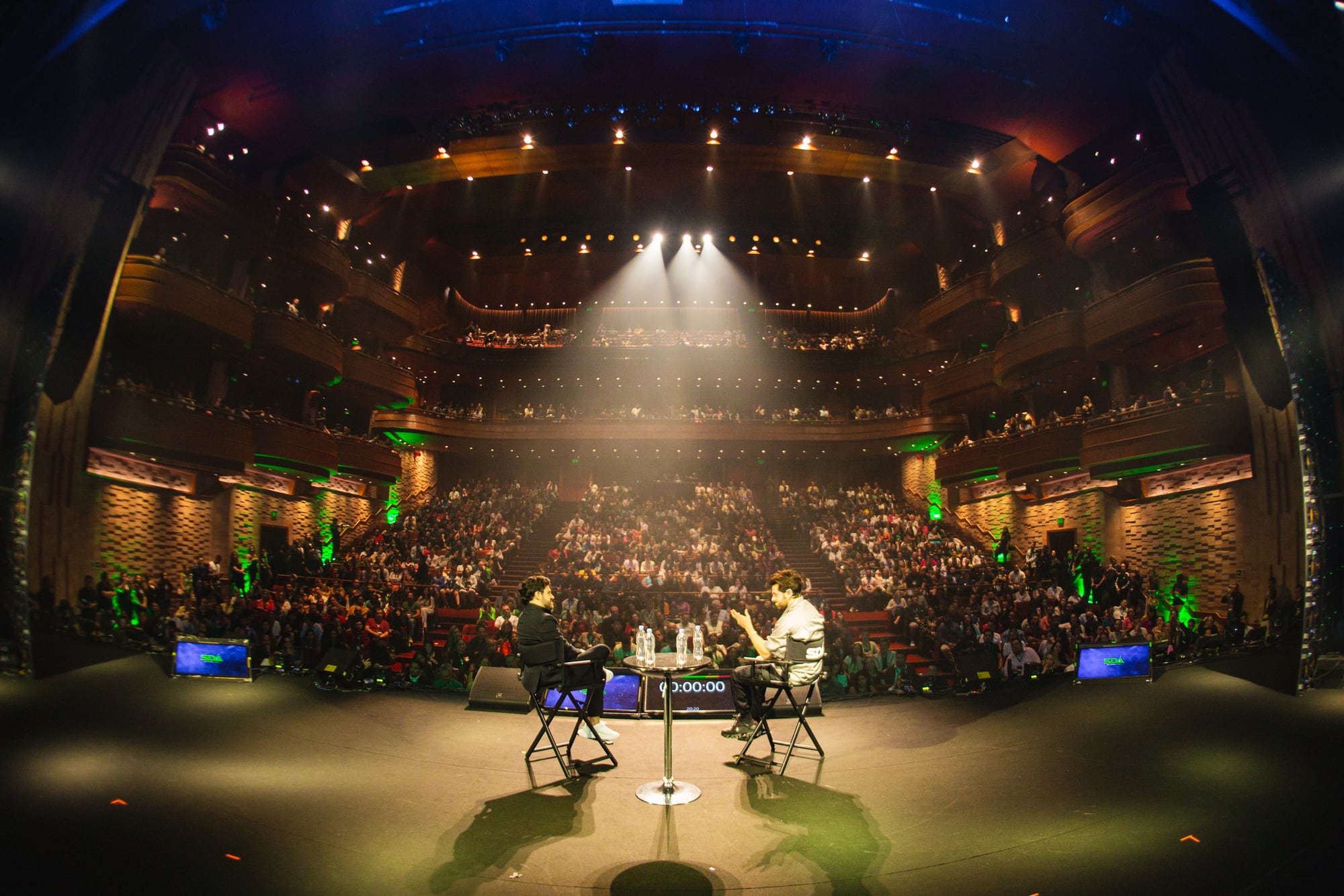Vista do palco durante uma conversa no evento, com o teatro cheio ao fundo
