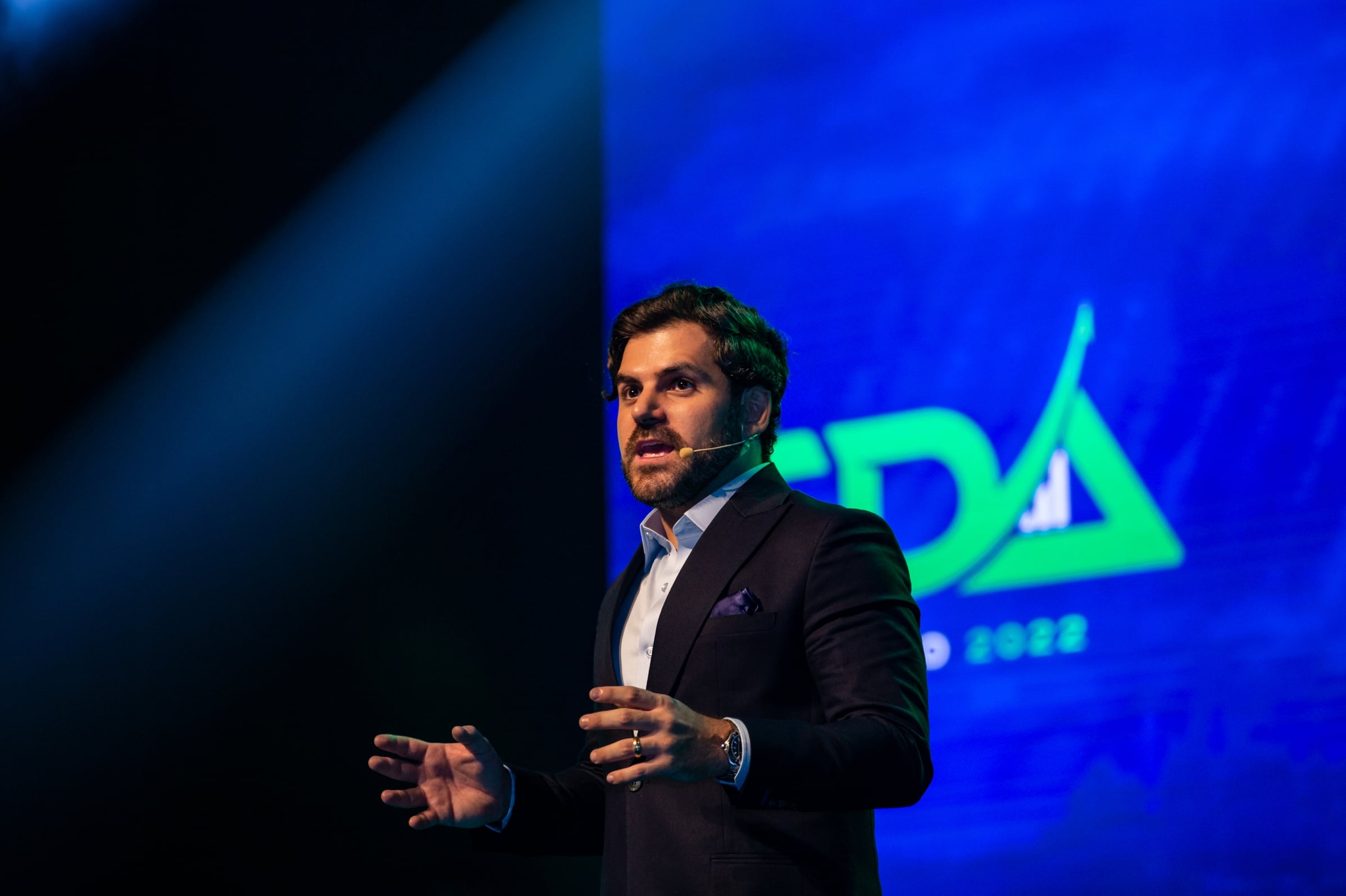 Samuel Pereira no palco do SDA Ao Vivo, com o logo do Segredos da Audiência ao fundo